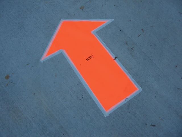 a large orange arrow taped to the ground, with the very small word 'vote' written on it