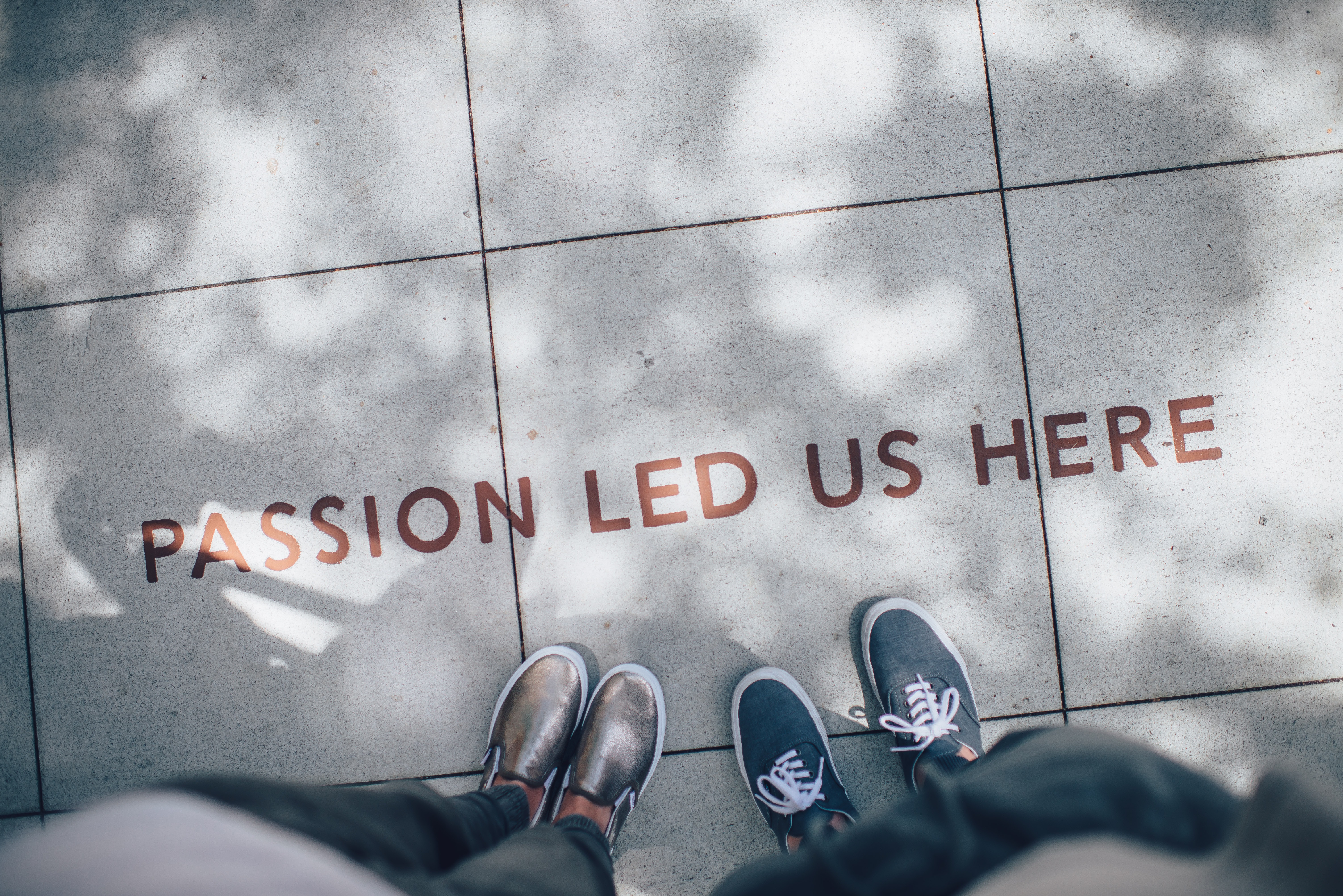 feet standing on sidewalk painted with "passion led us here"