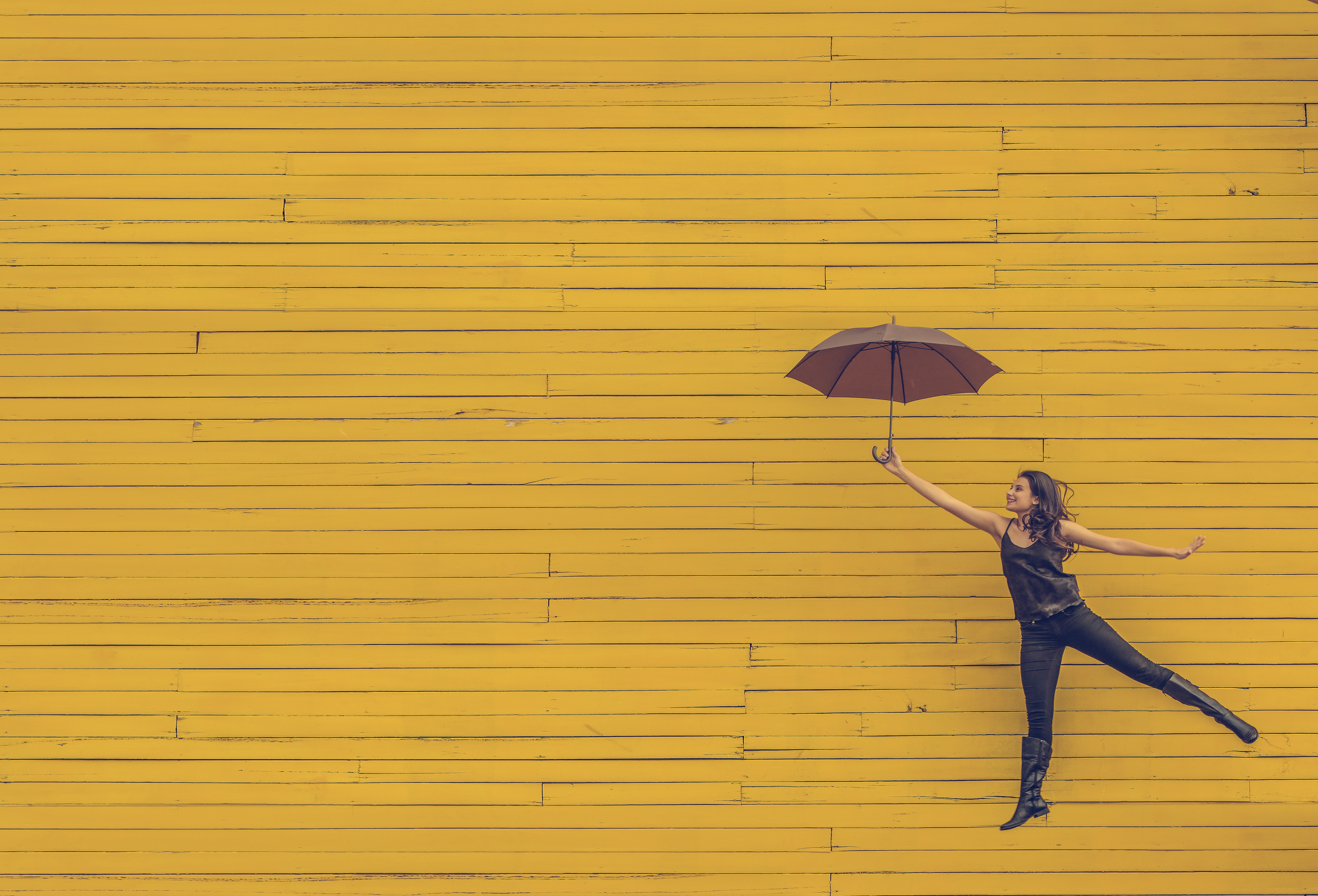 woman with umbrella in air against yellow wall
